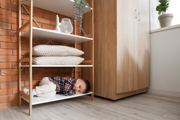 Little boy lying on shelf at home. Child in danger