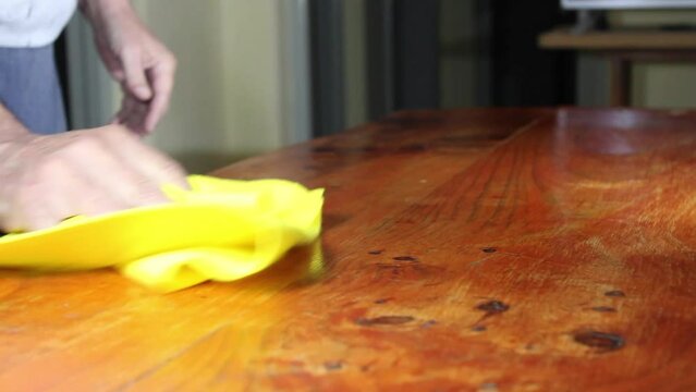 Limpieza en el hogar con el trapo absorvente amarillo antibacterias en la mesa de la cocina, el hombre pasa el trapo sobre el mueble de madera para la higiene y limpieza de la casa.  