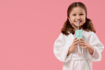 Happy little girl with oral irrigator on pink background