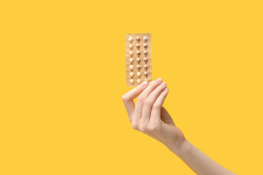 Female hand with birth control pills on yellow background