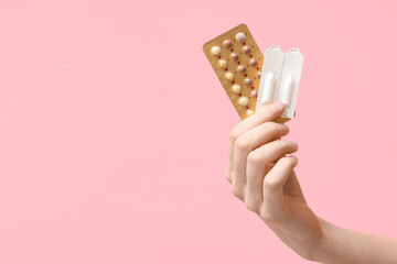 Female hand with birth control pills and vaginal suppositories on pink background