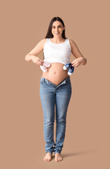 Young pregnant woman with baby booties on brown background