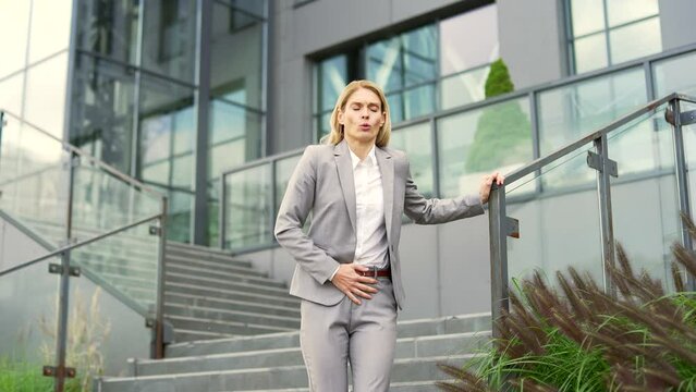 Sick businesswoman suffering from stomach pain while walking outside down stairs of office building. Upset woman has gastritis, poisoning, digestive problems, constipation, convulsions or menstruation