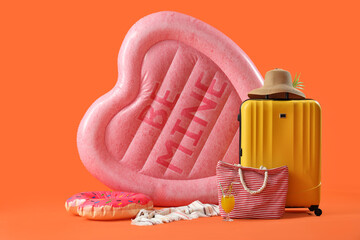 Swimming mattress in shape of heart with suitcase, bag and towel on orange background