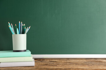 Pencil holder full of pencils and books on table against green background. End of school