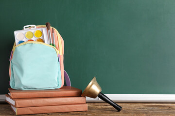 Backpack with art supplies on table against blackboard