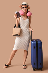 Young happy woman in sunglasses and hat with passport and suitcases on beige background