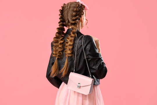 Beautiful young woman in leather jacket with braids and handbag on pink background