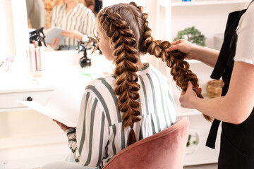 Professional hairdresser braiding client's hair in salon
