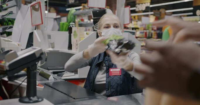 Female cashier wearing face mask scanning products and giving food to customer working at counter during pandemic. Shopping and retail business concept.