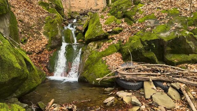 The old picturesque waterfall is covered with green moss and is pleasing to the eye, but nearby there are huge wheels of a tractor truck - bad traces of civilization