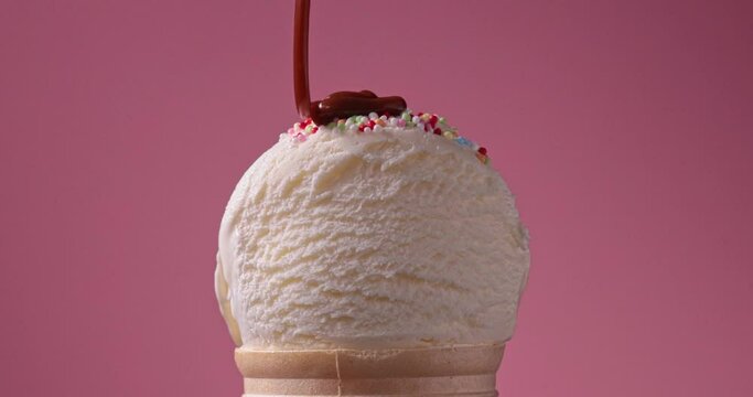 chocolate sauce flowing on vanilla ice cream scoop in waffle cone close up