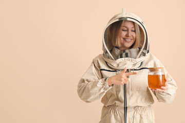 Female beekeeper pointing at jar of sweet honey on beige background