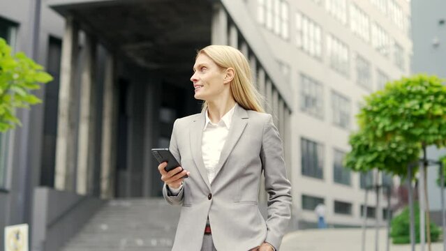 Happy businessman in formal suit is using a phone while walking on the street near an office building. Female manager reading writes a text message chatting, texting, checking email or browsing online