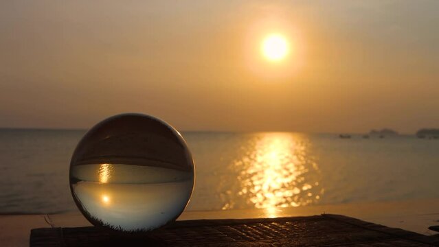Crystal ball on sunset sea beach with reflection of sun inside. Idyllic tranquil evening landscape