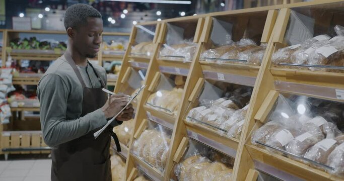 African American man supermarket manager counting bread and writing doing inventory in retail store. Greengrocer's and accounting concept.