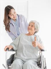 Fototapeta premium Asian doctor drive a wheelchair, old patient show thumb up sign with hand, doctor and old female talk about symptoms and treatment plan, rehabilitation activity, elderly healthcare promotion