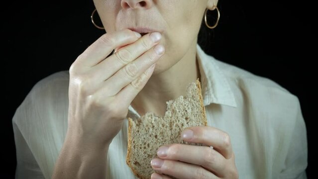 Sad woman suffer from malnutrition. A young woman suffer from malnutrition and eating bread against black background.