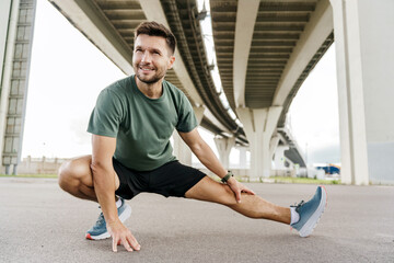 An athletic man stretches before a run, exemplifying dedication to health under an overpass, pairing green shirt with determination.