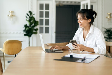 An engaged businesswoman multitasks, seamlessly integrating technology as she uses her smartphone...