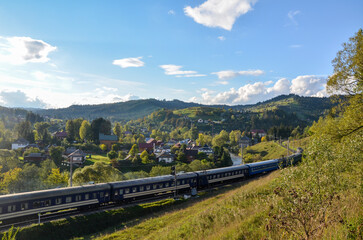 Train traveling along tracks that cut through the scenic countryside terrain with rolling hills covered in lush greenery in Vorokhta village, Carpathian Mountains, Ukraine