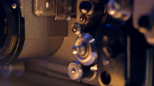 Close-up shot of vintage 16mm film projector reels with blue and yellow lights. Screening classic movies on mid-century film technology. Rotating shiny silver film spools for nostalgic cinematic.