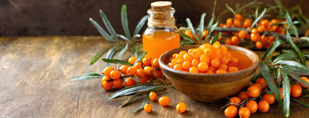 Golden Berries of sea buckthorn and nectar in glass bottle. A Rustic Still Life. Earthen bowl overflows with vibrant, fresh edible orange fruits. - obrazy, fototapety, plakaty