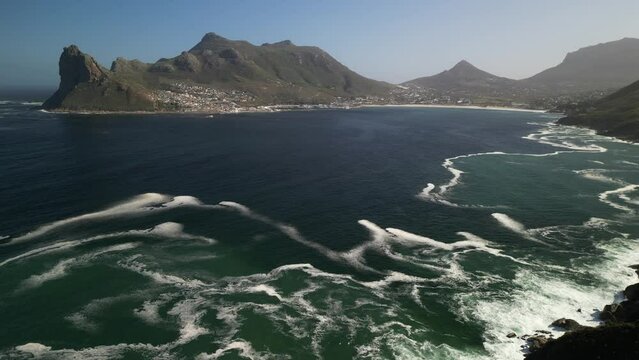 An aerial perspective reveals the stunning natural beauty of Hout Bay, showcasing the tranquil sea, rugged coastline, and surrounding mountains bathed in sunlight