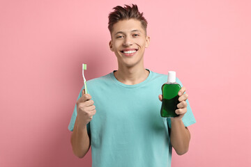 Young man with mouthwash and toothbrush on pink background