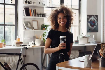 Foto op Plexiglas A woman with curly hair is smiling and holding a coffee cup. The room has a cozy and welcoming atmosphere, with a bicycle leaning against the wall and a laptop on the table © Sascha