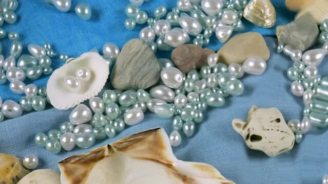 Imitation of the seabed. Oyster and scallop shells, sea pebbles and pearls on a background of blue and beige fabrics under water. Ripples on the surface of clear water.