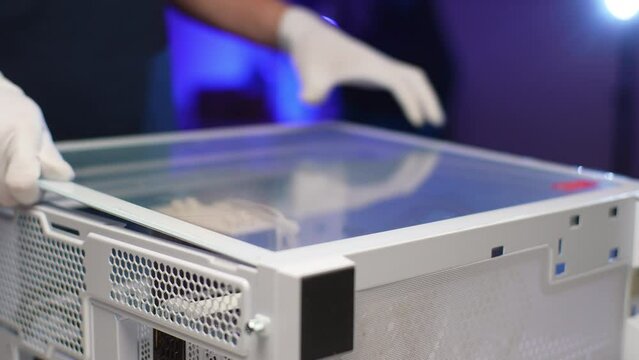 Computer technician male in gloves assembling PC system unit, installing transparent cover in dark workshop with neon blue light. Concept of computer hardware, upgrade and technology, slow motion.