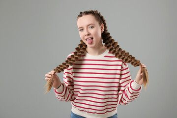 Woman with braided hair showing tongue on grey background