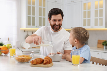 Father and his cute little son having breakfast at table in kitchen