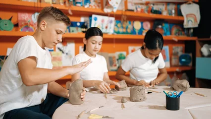 Fototapete Rund Caucasian smart teenager modeling clay while craving glass of clay at art lesson. Group of multicultural happy student working at dough in pottery workshop. Creative activity concept. Edification. © Summit Art Creations