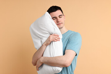 Man in pyjama holding pillow and sleeping on beige background