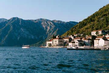Fototapeta na wymiar Boats float on the sea off the coast of Perast at the foot of the green mountains. Montenegro