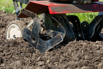Garden tiller tilling soil in spring. Gardening, soil health and fertility concept. 