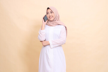 girl indonesia muslim wearing a hijab, candid, cheerful smile, holding a cellphone gadget in her hand while calling someone. Lifestyle, technology and promotion concept