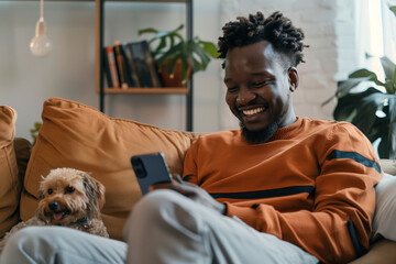 Happy Black Man Looking at and Using Smartphone at Home with Cute Dog - obrazy, fototapety, plakaty