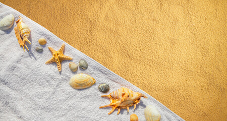 Top view of a beach with towel and seashells on the sand under the hot summer sun. Concept of sandy beach holiday, flat lay, background with copy space for text