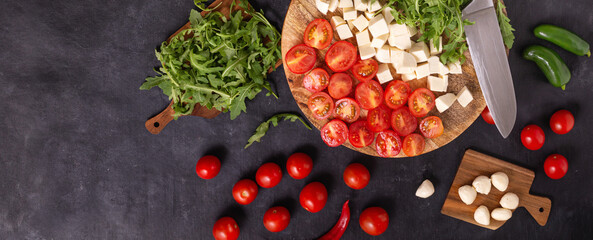 Top view of salad ingredients with mozzarella cheese, tomatoes and herbs on a wooden chopping board, flat lay, horizontal banner with space for text