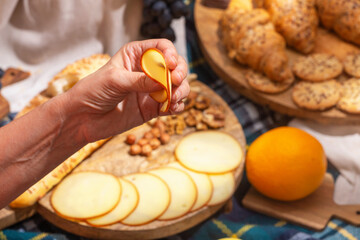 Close-up of hand holding cheese against a background of laid out picnic food, selective focus. The concept of summer outdoor recreation on the weekend