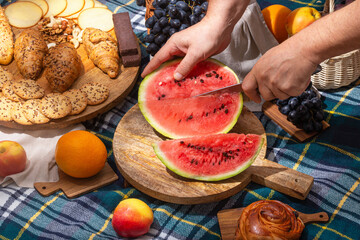 Close-up view of a cut watermelon in hands and laid out food for a picnic, selective focus. The concept of summer outdoor recreation on the weekend