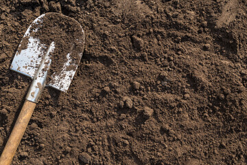 Brown soil ground texture background with copyspace and shovel on garden bed in farm garden....