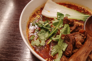 A vibrant bowl of Spicy Beef Noodle Soup, featuring succulent braised beef in a fiery broth,...
