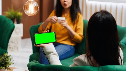 Asian traveler using smartphone with blank greenscreen at hotel, looking at template with chromakey...