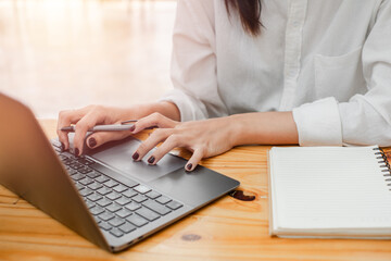 Close-up of a woman hands typing on a laptop keyboard, notebook beside her, indicating focused work.