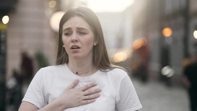 Worried young woman walking down the urban street while has panic heart attack hold hand on chest and try to calm down alone Anxious female with mental health problem outdoors