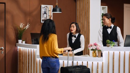 Asian hotel staff greeting customer at front desk entrance, welcoming female client and ensuring...